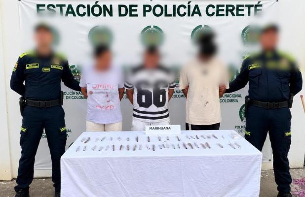 dos funcionarios policiales con tres personas capturadas, frente a ellos una mesa con elementos estupefacientes incautados