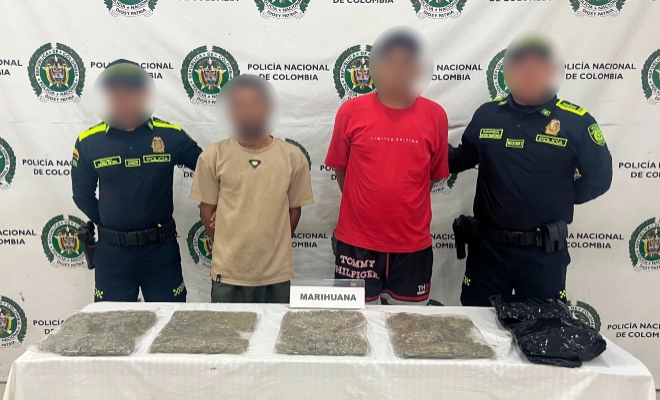 Dos funcionarios policiales con dos ciudadanos capturados frente al pendón institucional frente a una mesa con material incautado