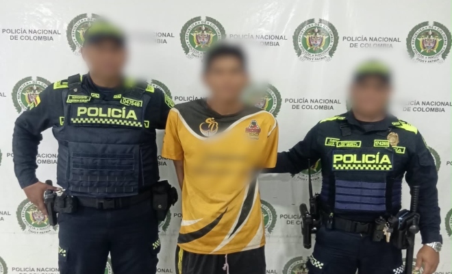 Dos funcionarios policiales con un ciudadano capturado frente a pendón institucional 
