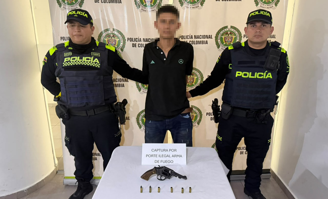 dos policías con un capturado y un revolver con munición sobre la mesa.