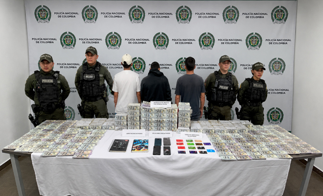 Se observa cuatro uniformados de la Policía Nacional con tres personas capturadas una mesa que tiene sobre ella más de 7 millones en papel moneda extrajera cuatro celulares y dos libretas de anotaciones