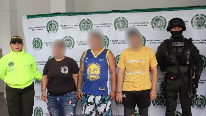 Tres personas, presuntamente capturadas, son sostenidas por dos Policías.