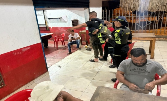un policia registrando a un ciudadano y un policia prestando seguridad 