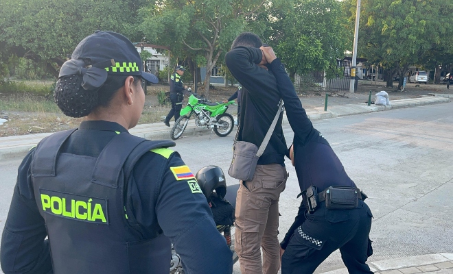 Tres funcionarios policiales realizando registro a persona a un ciudadano al lado de una motocicleta 