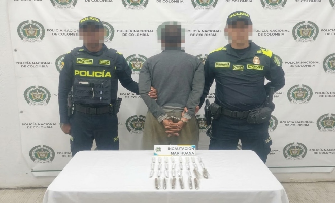 Dos funcionarios policiales con un ciudadano capturado frente a pendón institucional frente a ellos una mesa sobre la cual esta el material incautado 