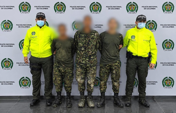 Dos policías custodiando tres personas capturadas