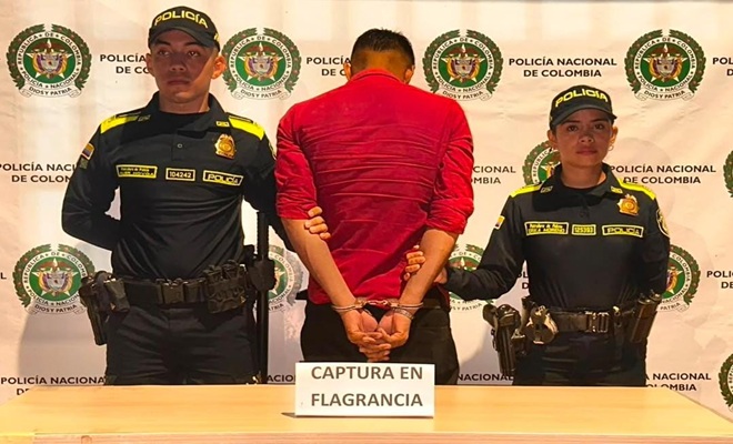 Dos policías custodiando el sujeto capturado frente al backing