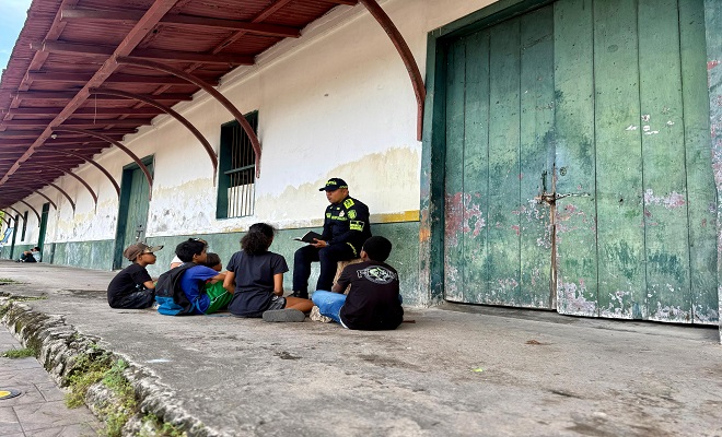 Un policía del grupo de infancia y adolescencia se encuentra realizando la lectura de un libro para unos niños que lo acompañan 