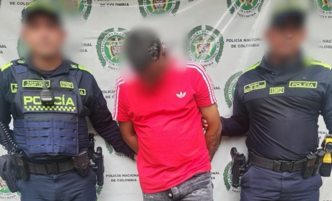 Dos funcionarios policiales con un ciudadano capturado frente a pendón institucional 