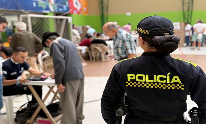 una uniformada de la Policía Nacional, varios ciudadanos, varias mesas y puestos de votación 