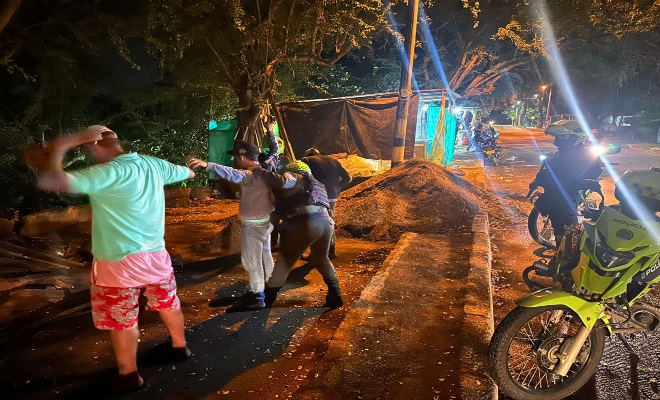 Dos policitas registrando a tres ciudadanos y un policia prestando seguridad 