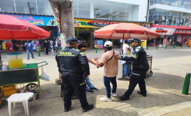 Un policía registrando a dos ciudadanos y un policía prestando seguridad 