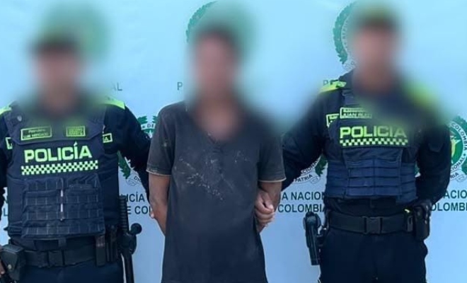 Dos funcionarios policiales con un ciudadano capturado frente a pendón institucional 