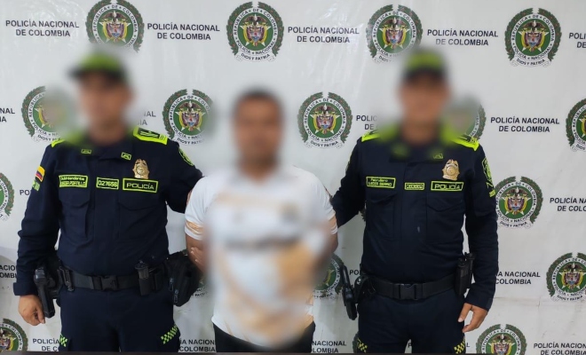 Dos funcionarios policiales con un ciudadano capturado frente a pendón institucional 