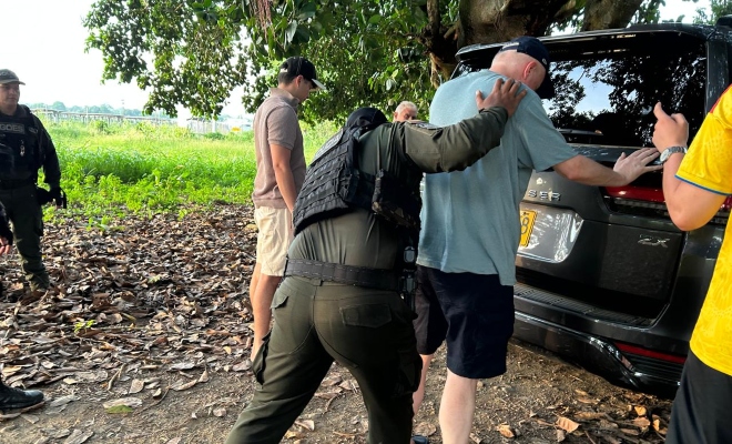 Funcionario policial realizando registro a persona a un grupo de tres ciudadanos junto a una camioneta color gris