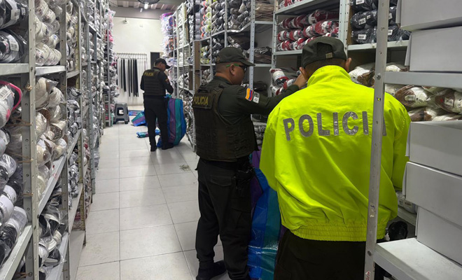 Un funcionario de policía judicial y un uniformado de la policía fiscal y aduanera inspeccionan varios pares de calzado de procedencia ilegal hallados en el inmueble