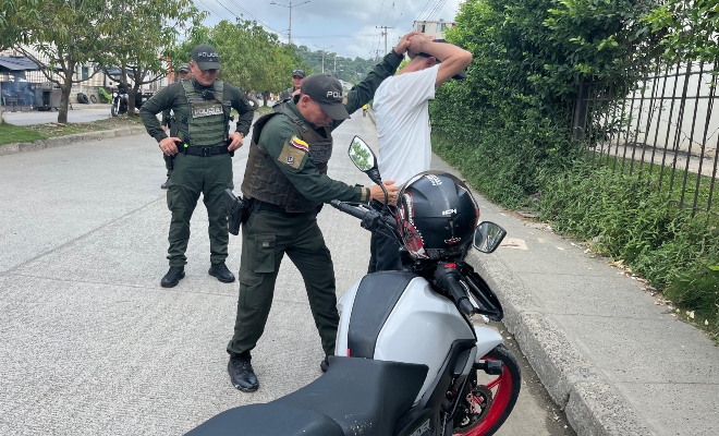 Dos funcionarios policiales realizando un registro a persona a un ciudadano junto a una motocicleta