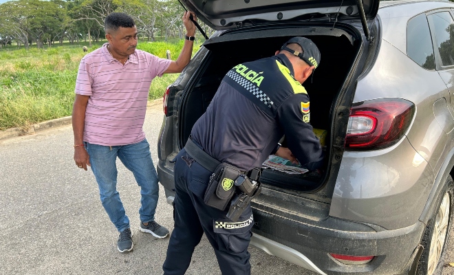 Funcionario policial junto a un ciudadano realizando registro a vehículo 