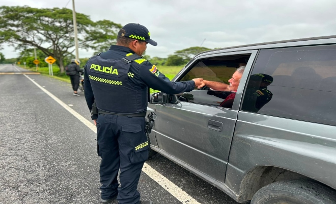 un uniformado de la Policía nacional  saludando a un ciudadano que se desplaza en su vehículo 