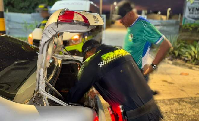 Funcionario policial realizando registro a vehículo color gris junto a un ciudadano 