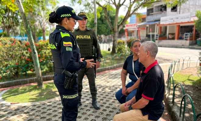 Una funcionaria policial y auxiliar de policía hablando con dos ciudadanos en parque brindando recomendaciones de seguridad