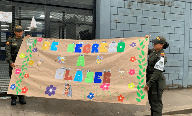 Dos auxiliar de policía sosteniendo un cartelera con el lema regreso a clase