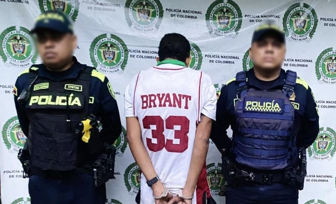 Dos funcionarios policiales con un ciudadano capturado frente a pendón institucional 