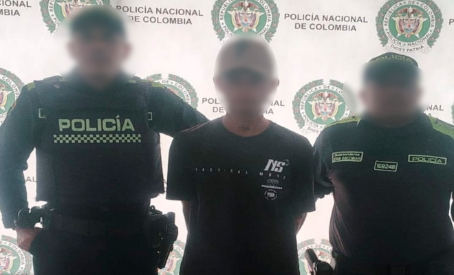 Dos funcionarios policiales junto a un ciudadano capturado frente a pendón institucional