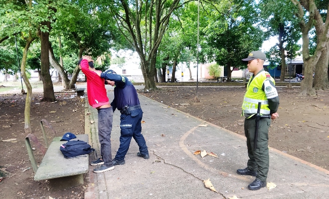 Dos funcionarios policiales realizando registro a ciudadano en un parque 