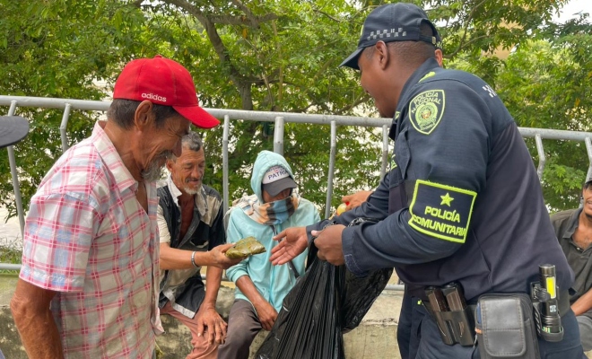 Funcionario policial entregando alimento a un grupo de ciudadanos en condición de habitante de calle 