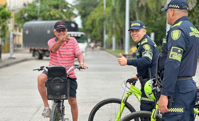 Dos funcionarios policiales del grupo de turismo en bicicletas institucionales sonriendo junto a un ciudadano 