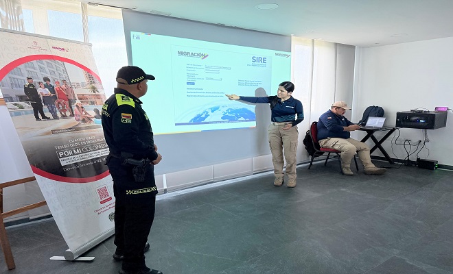 Uniformado del grupo de Turismo de la Policía Nacional en compañía de una funcionaria de Migración Colombia socializando el sistema SIRE mediante una pantalla 