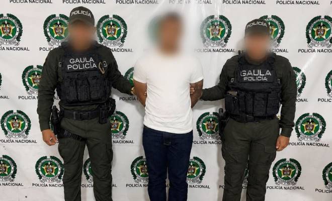 Dos uniformados del GAULA de la Policía Nacional custodian a una persona frente a un pendón institucional.