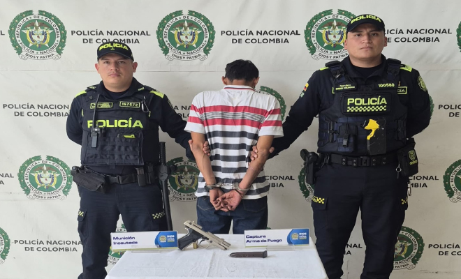 Hombre capturado en medio de dos Polic&iacute;as, en frente arma incautada