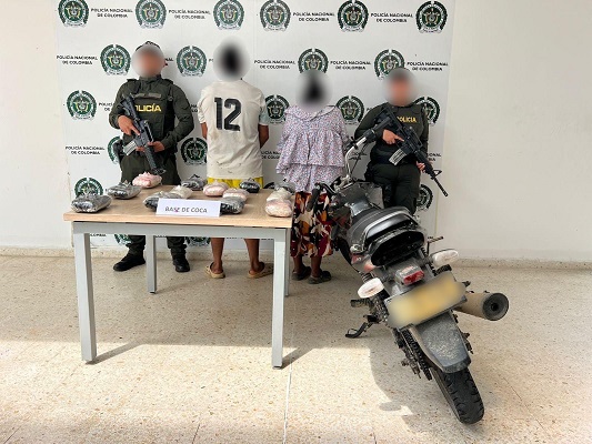 Dos personas capturadas junto a dos policías, una motocicleta y una mesa donde están los elementos incautados 