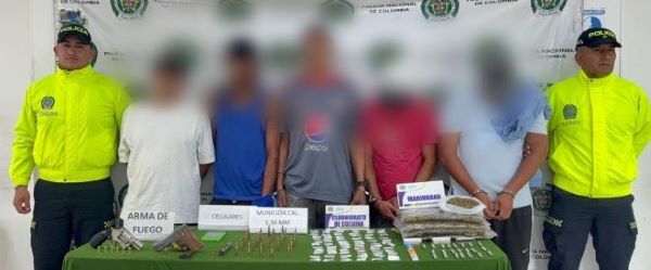 Dos policías al lado de cinco personas capturadas con material