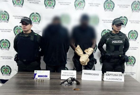 Dos policías al lado de dos hombres capturados por homicidio y un arma de fuego encima de una mesa