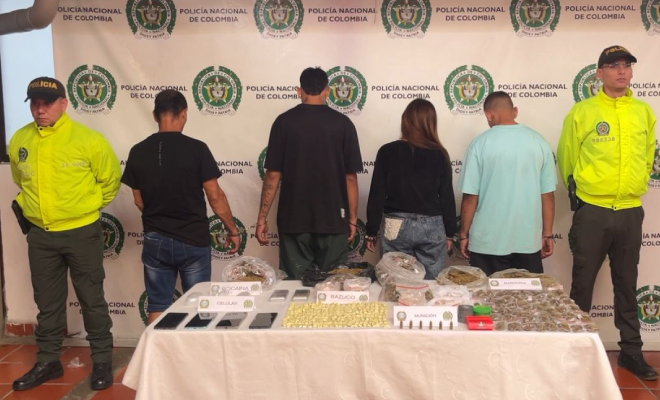 Personas capturadas en medio de dos Policías en frente se encuentra una mesa con elementos incautados