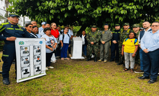 Agentes de la policía soldados y personal de la Fuerza Aérea junto a una cartelera varias personas con camisas de distintos colores están de pie frente a un muro blanco