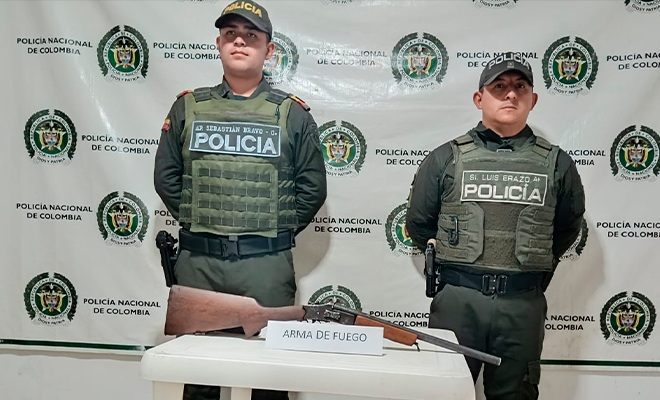 Dos policías con una escopeta incautada sobre una mesa
