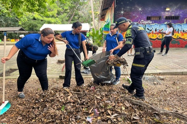 Un uniformado y tres funcionarias de la alcaldía participan en una jornada de limpieza, recogiendo hojas del suelo en el Malecón 