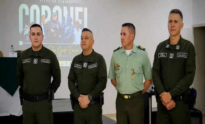 Cuatro uniformados están de pie en un evento institucional, frente a una pantalla de presentación.