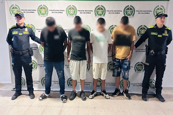 Dos uniformados custodian a cuatro hombres capturados por su presunta participación en actividades de tráfico local de estupefacientes 