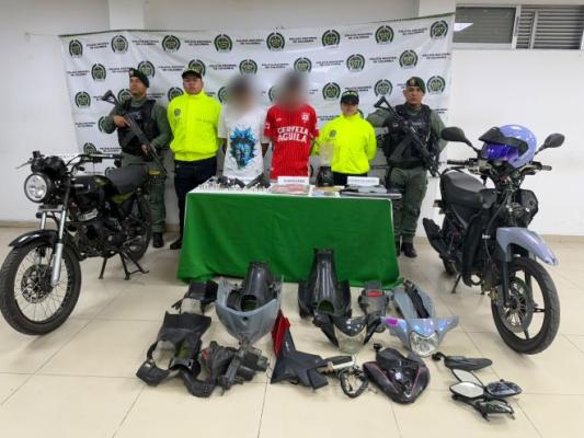 Policías al lado de dos hombres capturados con motocicletas, varias partes de motocicletas en el piso y dos motocicletas recuperadas.
